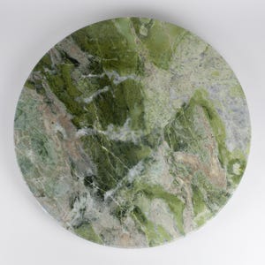 Op de afbeelding: Een cirkelvormige plaat van gepolijst groen marmer met een complex patroon van diep bosgroen, licht saliegroen en witte aders over het gehele stenen oppervlak. De natuurlijke minerale textuur vertoont gevarieerde organische vormen en kleuren.