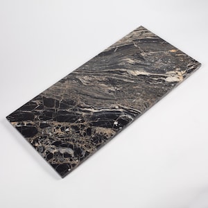 May include: A rectangular slab of polished black marble featuring intricate, swirling veins in shades of white, cream, and tan. The stone surface displays a high-gloss finish with a complex, natural pattern of fractured lines and organic mineral deposits.