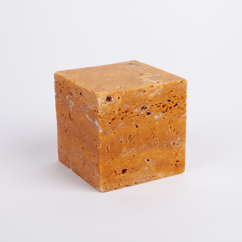 May include: A square, solid, yellow-brown travertine stone block with a rough, textured surface.