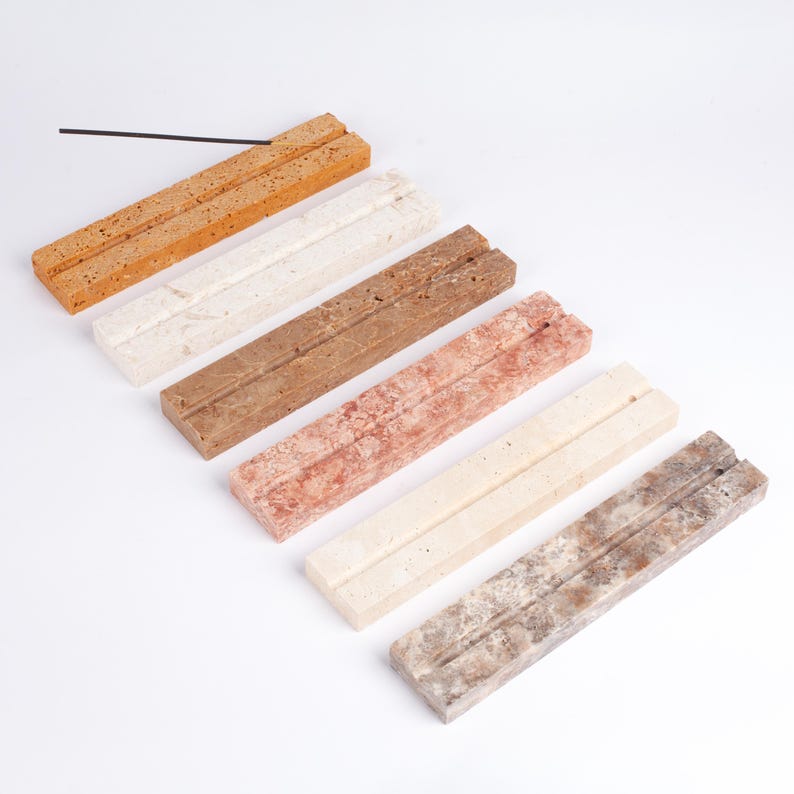 Pode incluir: Uma cole&ccedil;&atilde;o de seis suportes retangulares para incenso em v&aacute;rias cores, incluindo laranja, branco, castanho, vermelho, creme e cinzento. Cada suporte tem um sulco para segurar varetas de incenso. Uma &uacute;nica vareta de incenso preta &eacute; colocada no suporte laranja superior.