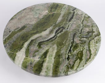 Puede incluir: Una mesa redonda de mármol verde con un patrón natural y arremolinado. La piedra presenta tonos de verde, gris y negro, creando un diseño único y orgánico. Ideal para una mesa pequeña o una superficie decorativa, con un diámetro de unos 60 cm.