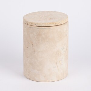 May include: A round, beige, stone container with a lid. The container has a rough, textured surface.