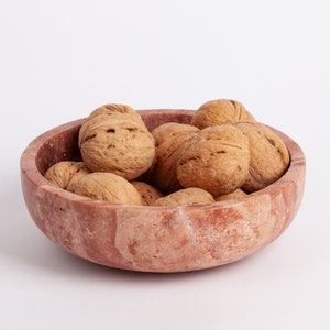 May include: A pink marble bowl filled with walnuts. The bowl has a natural, rustic look with visible veins and swirls.