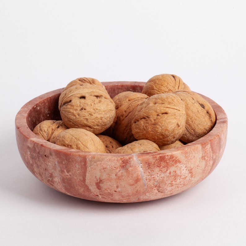May include: A pink marble bowl filled with walnuts. The bowl has a natural, rustic look with visible veins and swirls.