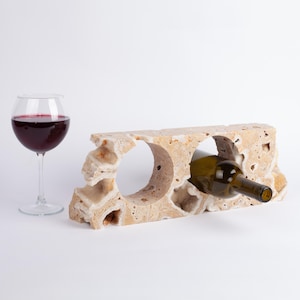 May include: A beige stone wine rack with two bottle holders. A bottle of wine is resting in one of the holders.