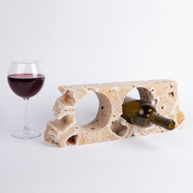May include: A beige stone wine rack with two bottle holders. A bottle of wine is resting in one of the holders.