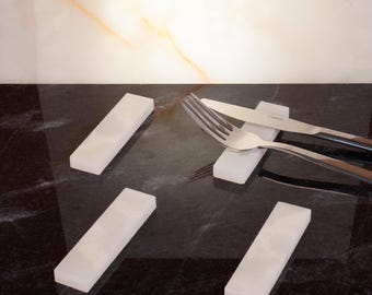 May include: A set of four rectangular white onyx knife rests. A fork and knife rest on one of the rests. The knife and fork are silver. The background is a black and white marble.