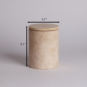 May include: A beige travertine stone container with a lid. The container is 5.1 inches tall and 3.7 inches in diameter.