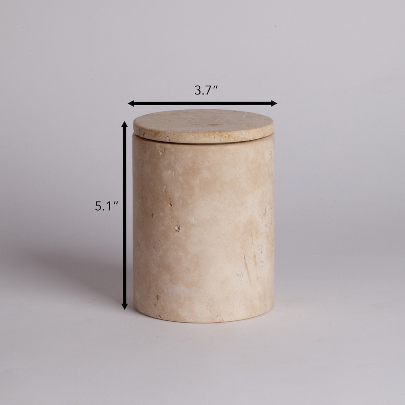 May include: A beige travertine stone container with a lid. The container is 5.1 inches tall and 3.7 inches in diameter.
