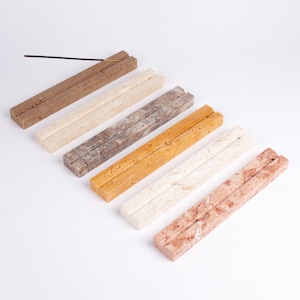 Könnte beinhalten: Eine Auswahl rechteckiger Räucherstäbchenhalter in verschiedenen Farben, darunter Braun, Creme, Grau, Orange, Weiß und Rot. Jeder Halter hat eine Nut zur Aufnahme von Räucherstäbchen. Ein Räucherstäbchen befindet sich im braunen Halter.
