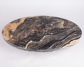 May include: Oval-shaped stone table with a polished surface. The table features a striking pattern of black, brown, and beige veining. The natural stone design adds a touch of elegance and sophistication to any space. The table measures approximately 60 inches in length.