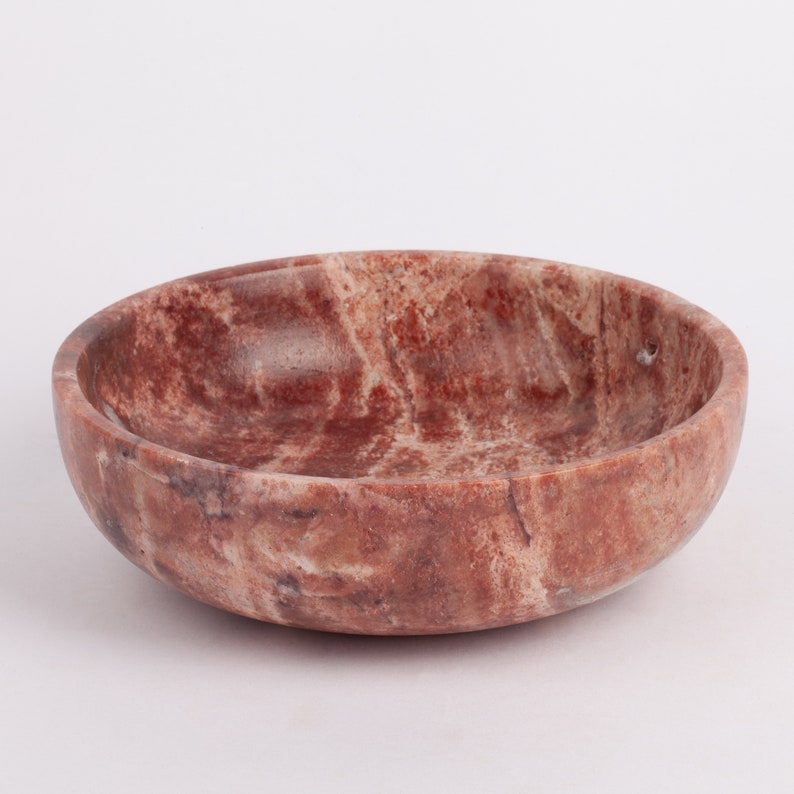 May include: A small, round, red and white marble bowl. The bowl has a smooth, polished surface and a slightly curved rim.