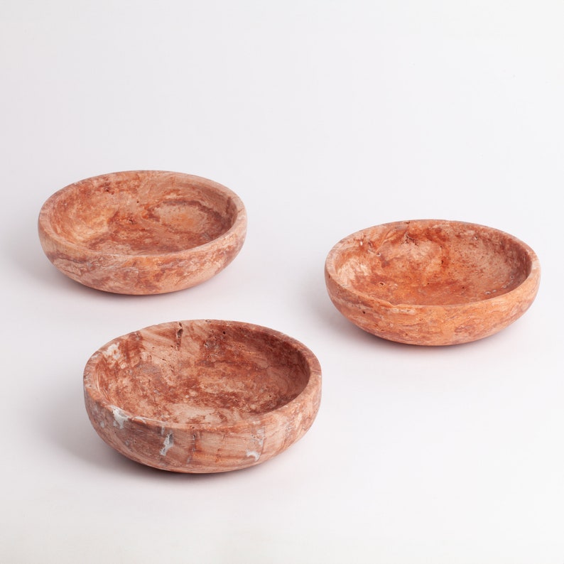 May include: Three round, brown, marble bowls with a mottled pattern. The bowls are arranged in a row on a white surface.
