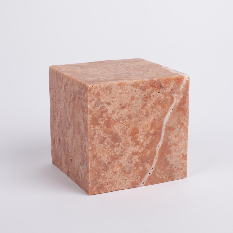 May include: A square, light pink, marble block with a white vein running through it.