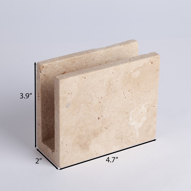 May include: A beige travertine stone napkin holder with a 3.9 inch height, 4.7 inch width, and 2 inch depth.