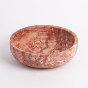 May include: A round, brown marble bowl with a white marbled pattern. The bowl is made of natural stone and has a rustic, handmade look.