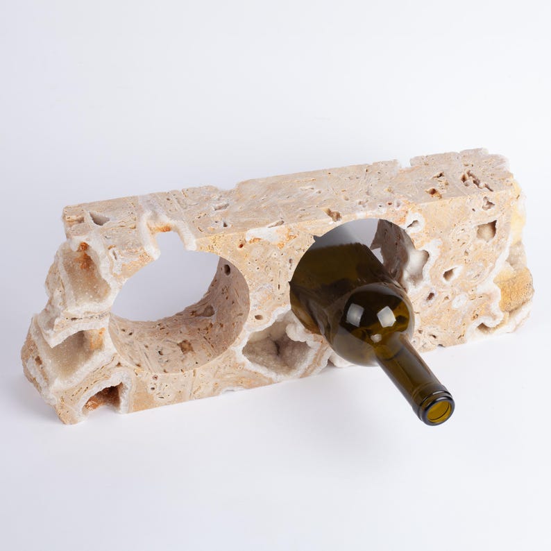 May include: A beige stone wine bottle holder with a bottle of wine in one of the slots. The holder has a rough, textured surface.