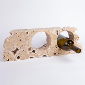 May include: A beige travertine wine bottle holder with two openings. One opening has a wine bottle in it.