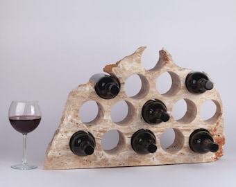 Puede incluir: Un estante de vino de piedra beige con 15 ranuras para botellas. El estante tiene forma de montaña y tiene una textura rugosa y natural.
