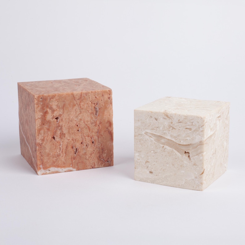 May include: Two square marble pedestals, one is a light brown color with darker brown veins and the other is a light cream color with white veins.