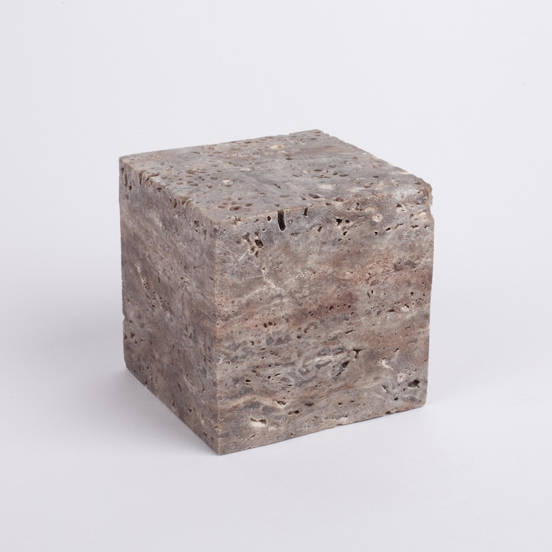 May include: A square, gray, stone pedestal with a rough, textured surface.