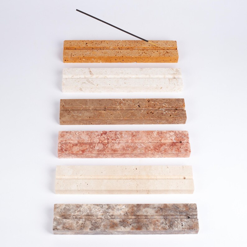 Pode incluir: Uma cole&ccedil;&atilde;o de porta-incensos retangulares em v&aacute;rias cores, incluindo bege, branco, castanho, vermelho, bege e cinzento. Cada suporte tem um sulco para segurar varetas de incenso. Uma vareta de incenso &eacute; colocada no suporte bege superior.