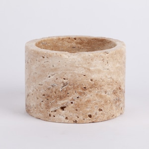 May include: A round, light brown travertine stone planter with a smooth, slightly textured surface. The planter is perfect for small plants or succulents.