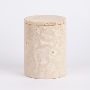 May include: A cylindrical beige marble storage container with a lid. The container has a natural, textured surface.