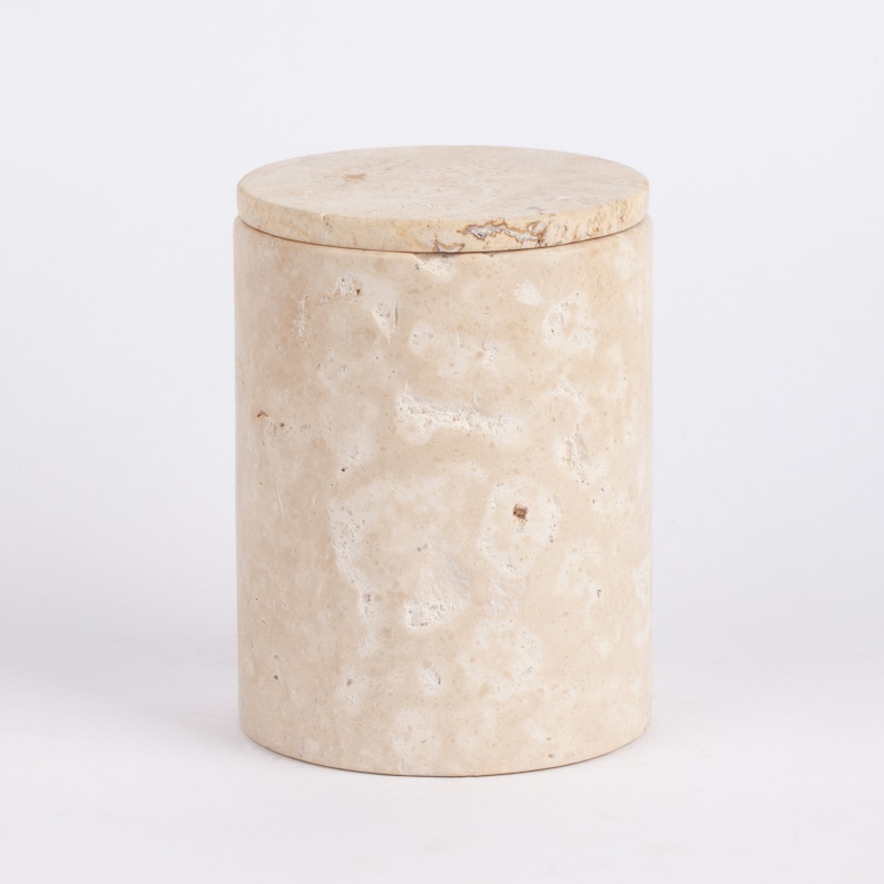 May include: A cylindrical beige marble storage container with a lid. The container has a natural, textured surface.