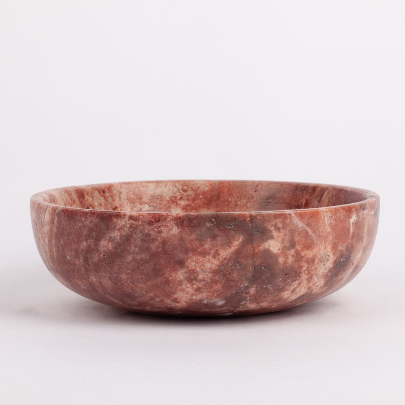 May include: A red and brown marble bowl with a smooth, rounded surface. The bowl is made of natural stone and has a unique, marbled pattern.