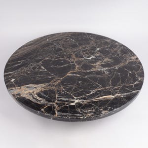 May include: A round, black marble tabletop with intricate veining in shades of gold and white. The polished surface reflects light, showcasing the natural patterns of the stone. This elegant piece is suitable for various home decor applications.