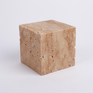 May include: A square, light brown, textured stone block.