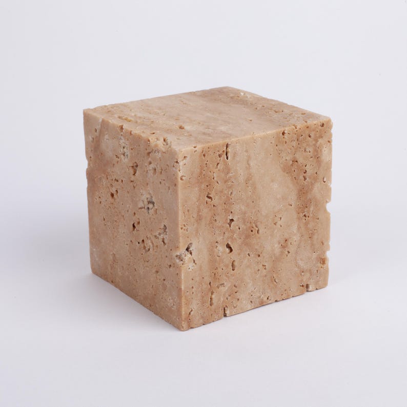 May include: A square, light brown, textured stone block.