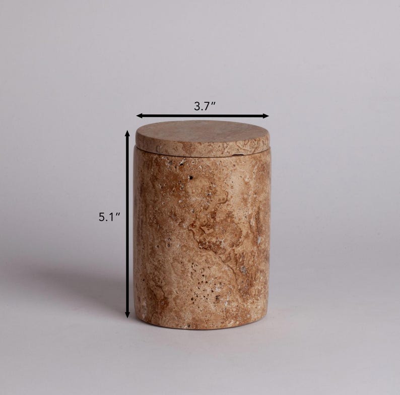 May include: A cylindrical, beige travertine stone container with a lid. The container measures 5.1 inches tall and 3.7 inches in diameter.