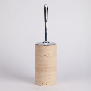 May include: A beige travertine toilet brush holder with a chrome handle.