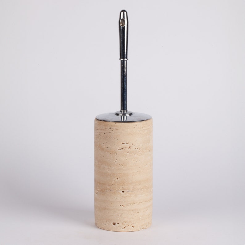 May include: A beige travertine toilet brush holder with a chrome handle.