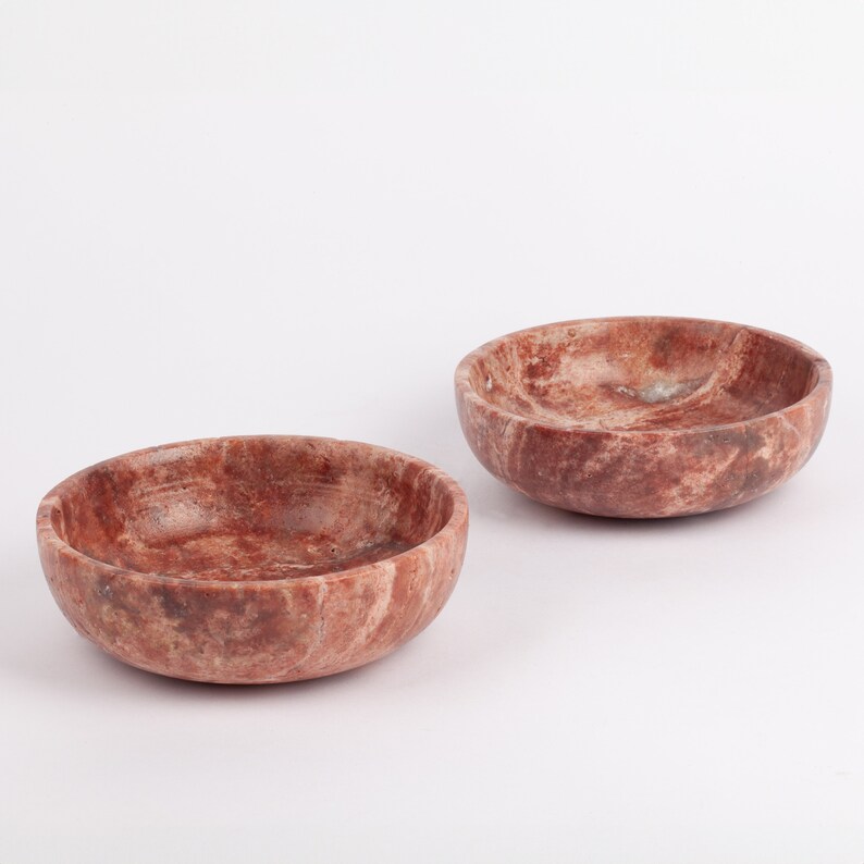 May include: Two small, round, red and white marble bowls. The bowls are made of natural stone and have a rustic, handmade look.