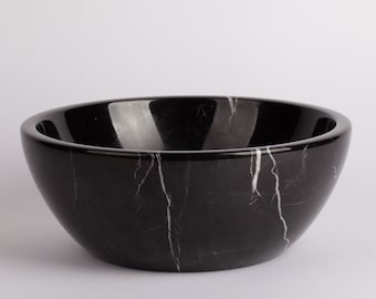 May include: A black marble bowl with white veining. The bowl is round and has a smooth, polished surface.