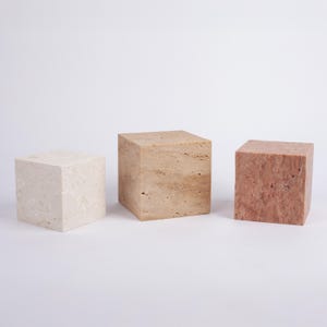 Puede incluir: Tres bloques decorativos cuadrados hechos de piedra natural. Los bloques son de diferentes tamaños y colores. El bloque de la izquierda es blanco, el bloque del medio es beige y el bloque de la derecha es rosa.