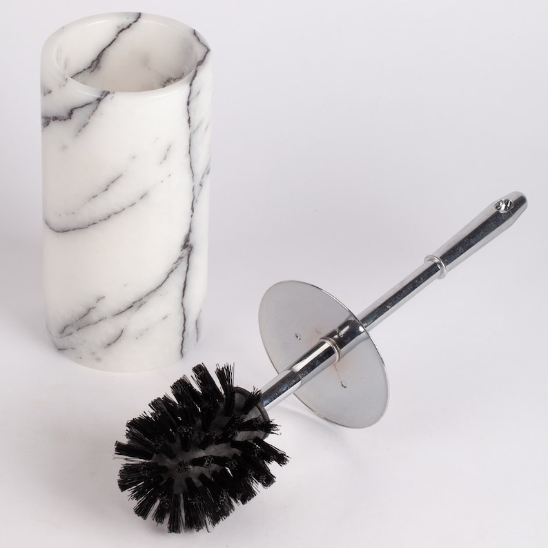 May include: A white marble toilet brush holder with a black toilet brush with a chrome handle and base.
