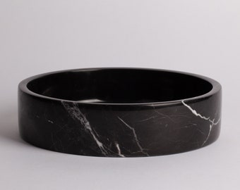 May include: A round black marble bowl with white veining. The bowl is shallow and has a wide rim.