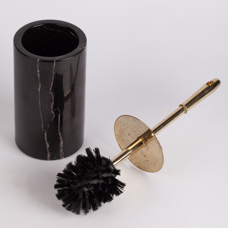 May include: A black marble toilet brush holder with a gold-colored toilet brush with black bristles.