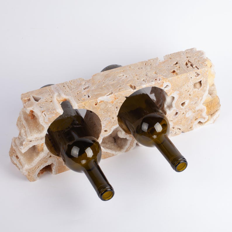 May include: A beige stone wine rack with two wine bottles in it. The rack is made of natural stone and has a rough texture. The bottles are brown glass and have a green tint.