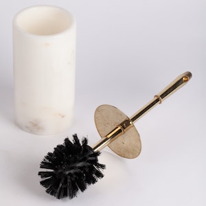 May include: A white marble toilet brush holder with a gold-toned toilet brush with black bristles.