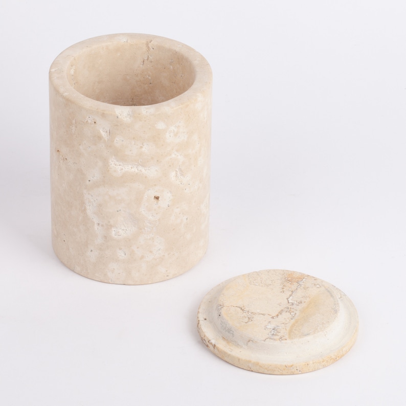 May include: A beige cylindrical container with a lid, both made of natural stone with a marbled pattern.