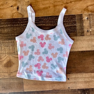 May include: White crop top with a pattern of pink, peach, and blue Mickey Mouse silhouettes. The tank top has a scoop neck and thin straps. The top is made of a soft, lightweight material.