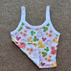 Puede incluir: Camiseta sin mangas blanca con un colorido estampado de frutas. El dise&ntilde;o incluye sand&iacute;a, kiwi, naranja y fruta del drag&oacute;n en un patr&oacute;n repetitivo. La camiseta sin mangas tiene tirantes y ribetes blancos.