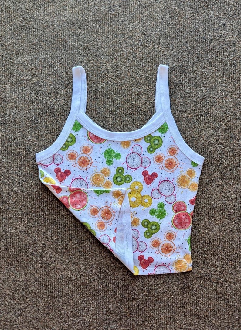 Puede incluir: Camiseta sin mangas blanca con un colorido estampado de frutas. El dise&ntilde;o incluye sand&iacute;a, kiwi, naranja y fruta del drag&oacute;n en un patr&oacute;n repetitivo. La camiseta sin mangas tiene tirantes y ribetes blancos.
