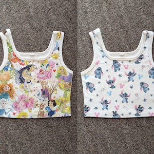 May include: Two white crop tops with a square neckline. One top features a colorful collage of Disney princesses and characters. The other top has a pattern of the character Stitch, with pink and blue accents, and stars.