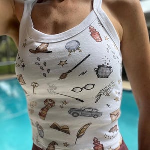May include: White tank top with a print of various Harry Potter themed illustrations, including a magic wand, a potion bottle, a flying car, and a golden snitch.